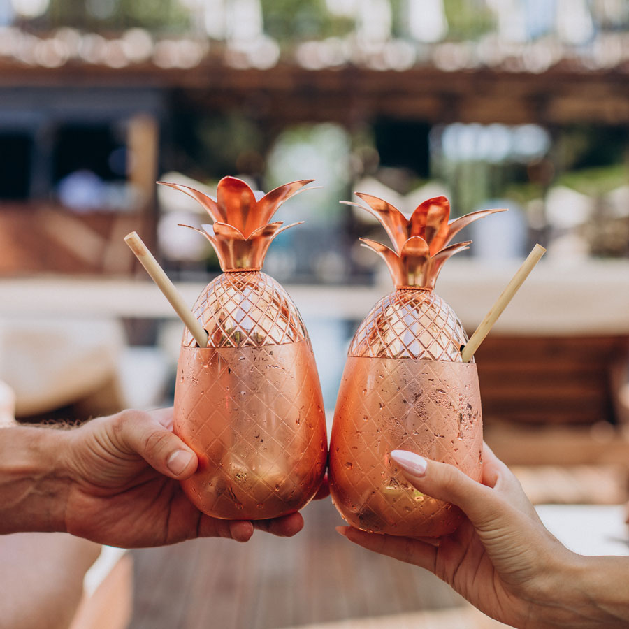 hands holding cocktails by pool